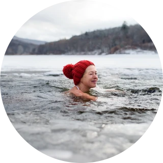 Eine Frau mit roter Mütze schwimmt in einem eiskalten See in winterlicher Landschaft